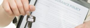 Hand holding a home key in front of a property insurance policy document in Thailand