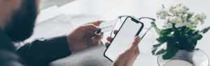 Man holding a credit card and smartphone – potential risk of online investment scams.
