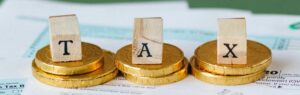 Taxes in Thailand for Expats: wooden blocks spelling 'TAX' on gold coins with tax documents in the background, symbolizing expatriate tax obligations.