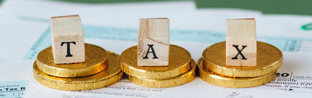 Taxes in Thailand for Expats: wooden blocks spelling 'TAX' on gold coins with tax documents in the background, symbolizing expatriate tax obligations.