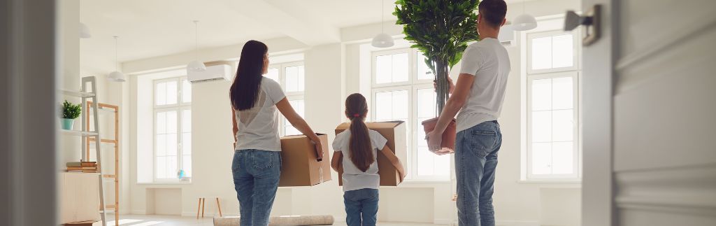 Une famille de trois personnes, composée d'une mère, d'un père et de leur fille, déménageant dans leur nouveau domicile en Thaïlande, portant des cartons et une plante.