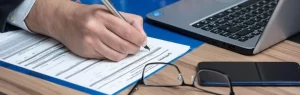 Remplissage d’un formulaire pour un visa non immigrant B Thaïlande, avec un ordinateur portable, un téléphone et des lunettes sur le bureau.