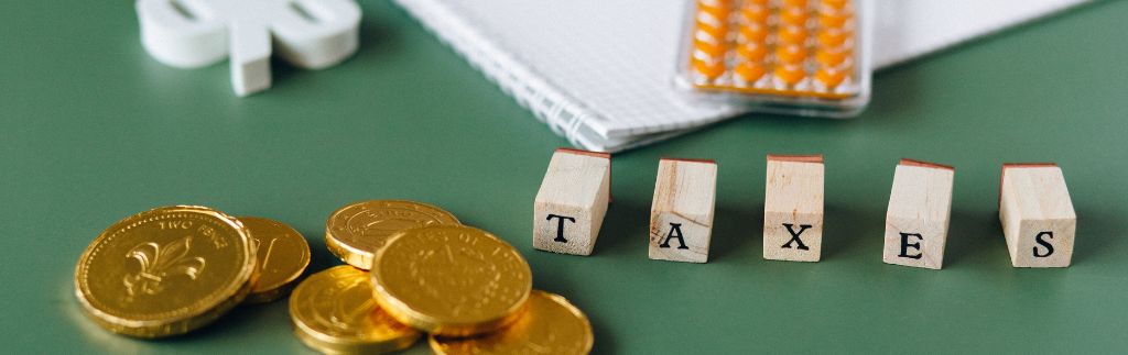 Wooden blocks spelling "TAXES" with gold coins on a desk, symbolizing the double taxation agreement Thailand.