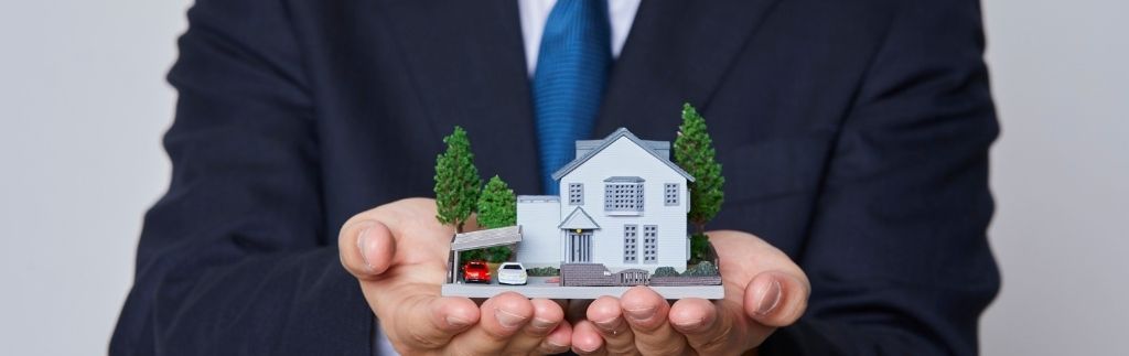 Immobilienmakler Thailand – professioneller Makler mit Modellhaus in den Händen