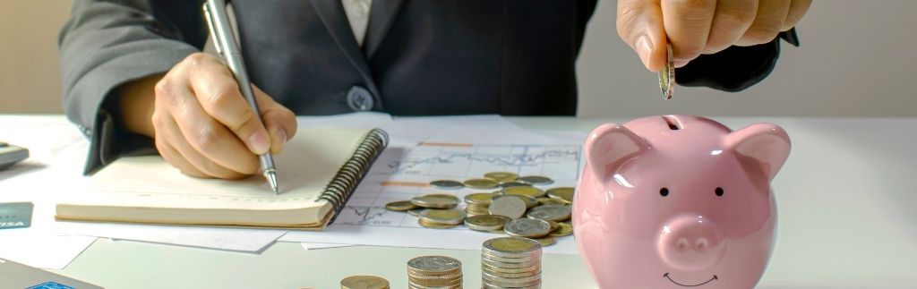 Personne en costume ajoutant une pièce dans une tirelire tout en gérant des documents financiers, illustrant les démarches pour ouvrir un compte bancaire en Thaïlande.