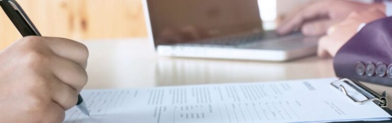 Une personne remplit le formulaire TM7 à la main devant un ordinateur portable, dans le cadre d’une demande d’extension de visa en Thaïlande.