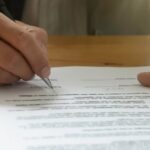 Person signing a TM7 Form document to extend a visa in Thailand.