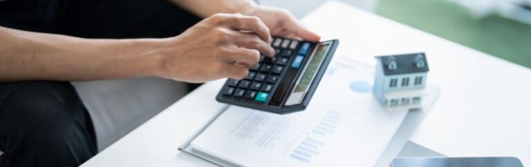 Persona che calcola documenti finanziari con una calcolatrice accanto a un modellino di casa, concetto legato alle tasse sulla casa in Thailandia.