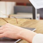 Mani di una persona che lavora al laptop e tiene un documento, immagine collegata al tema visa run Thailandia.