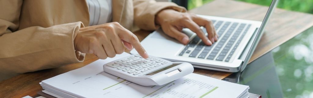 Personne utilisant une calculatrice et un ordinateur portable pour gérer des documents financiers, image liée au thème payer ses impôts en Thaïlande.